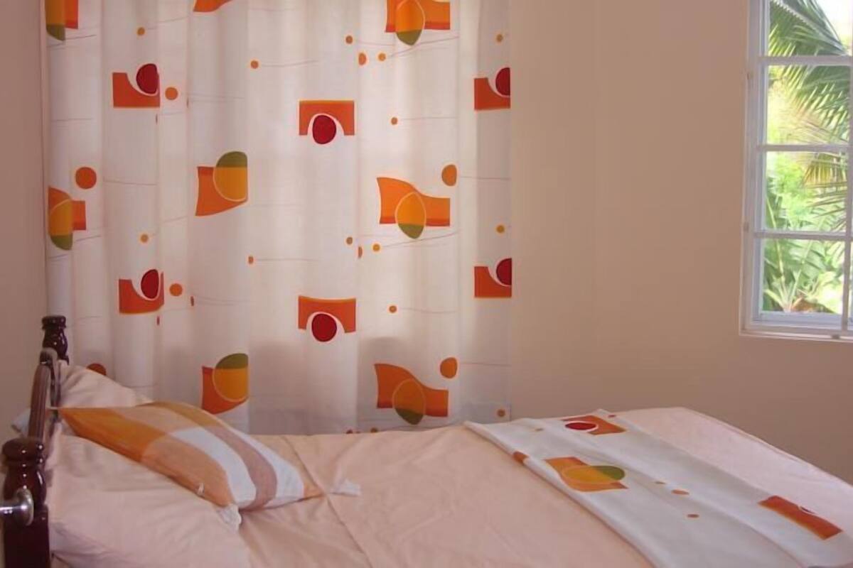 A room with a bed, a window with a view of greenery, and a curtain with abstract patterns.