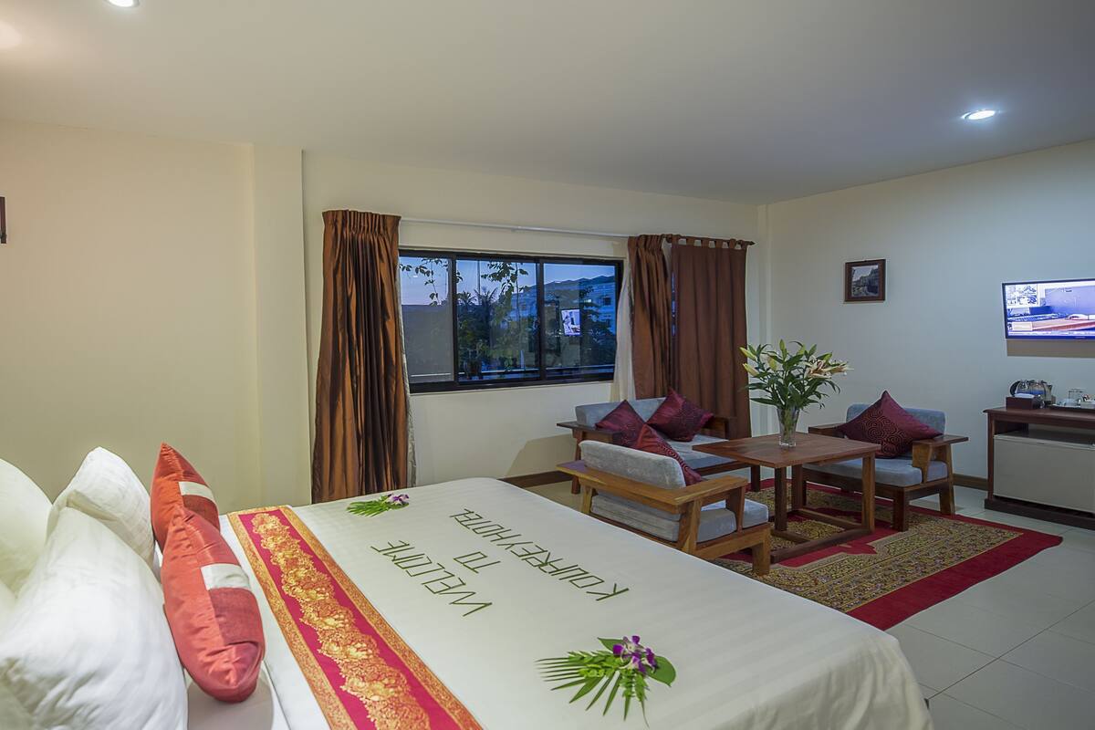 A hotel room with a bed, a desk, a chair, a TV, and a window with curtains.