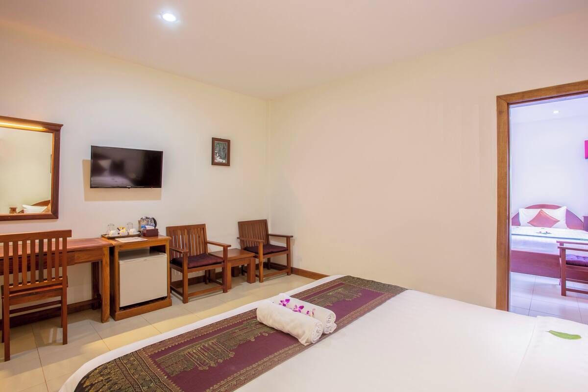 A hotel room with a bed, a desk, two chairs, a television, and a small table with a mirror.