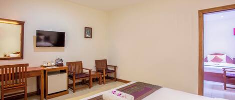 A hotel room with a bed, a desk, two chairs, a television, and a small table with items on it.