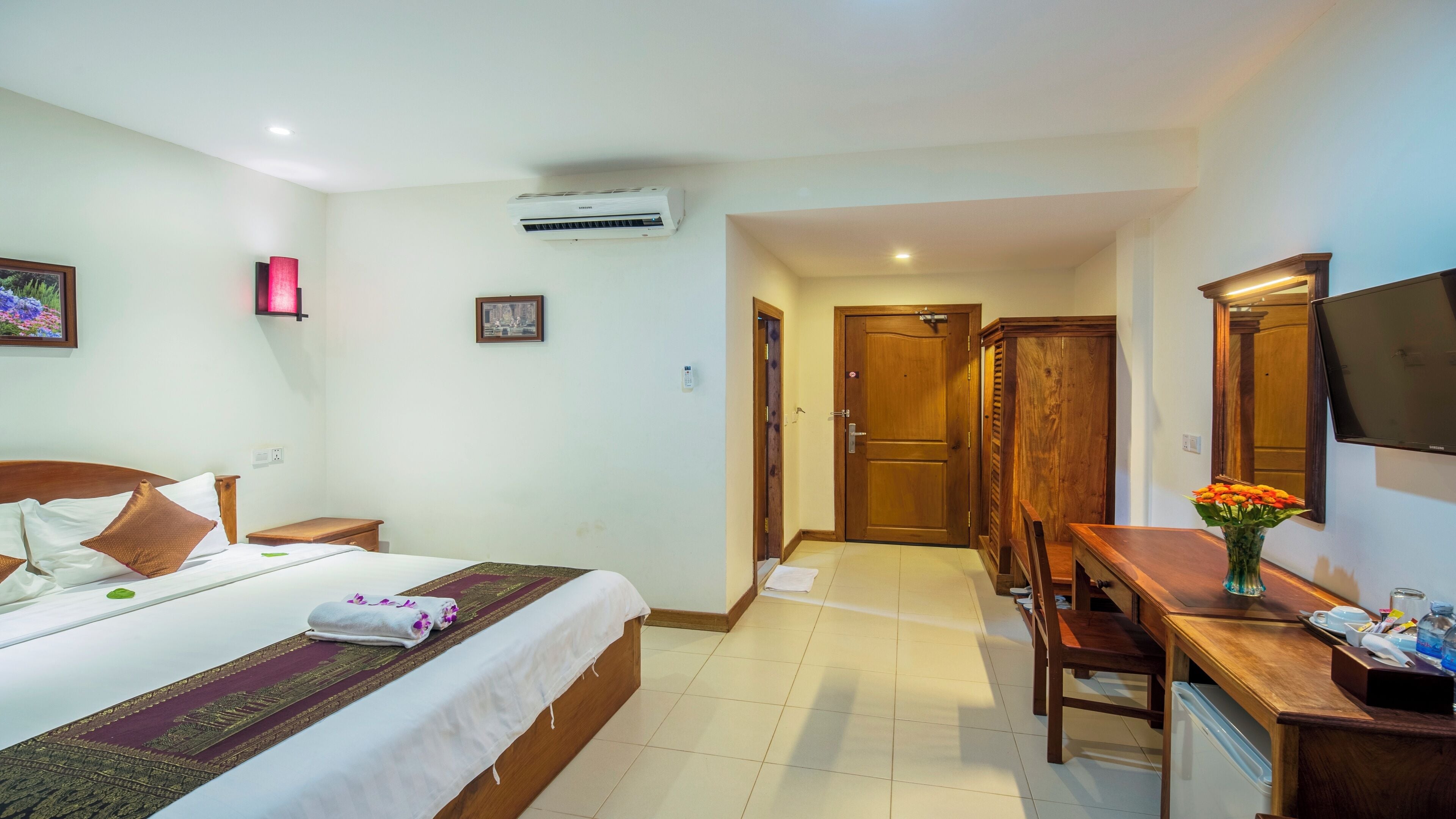 A hotel room with a bed, bedside table, desk, chair, and a TV on the wall.