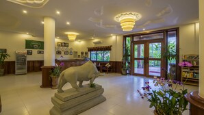 A lobby with a reception desk, a statue of a bull, a refrigerator, and a bookshelf. - Kouprey Hotel (Siem Reap)