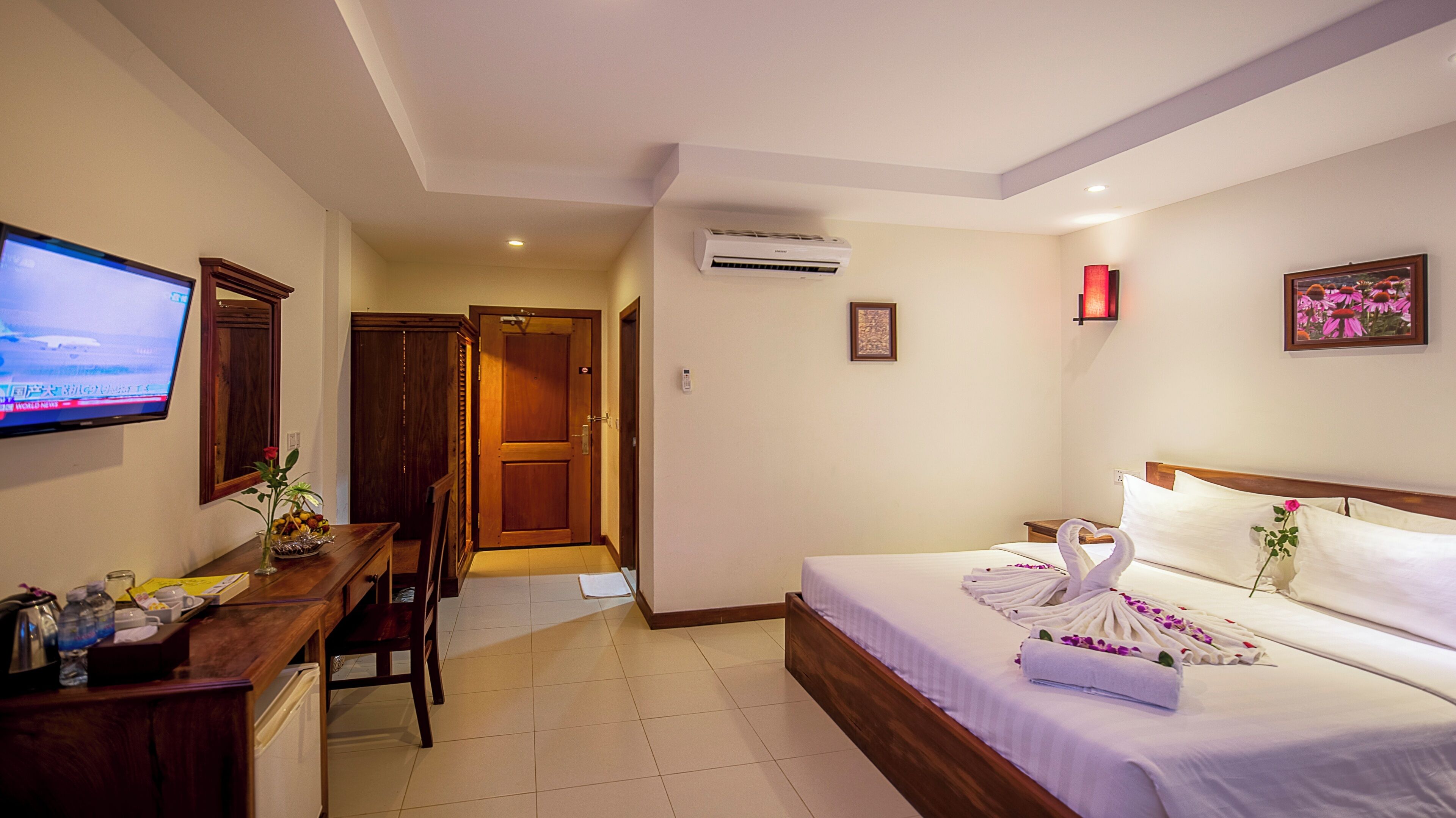 A hotel room with a bed, a desk, a television, and an air conditioning unit.