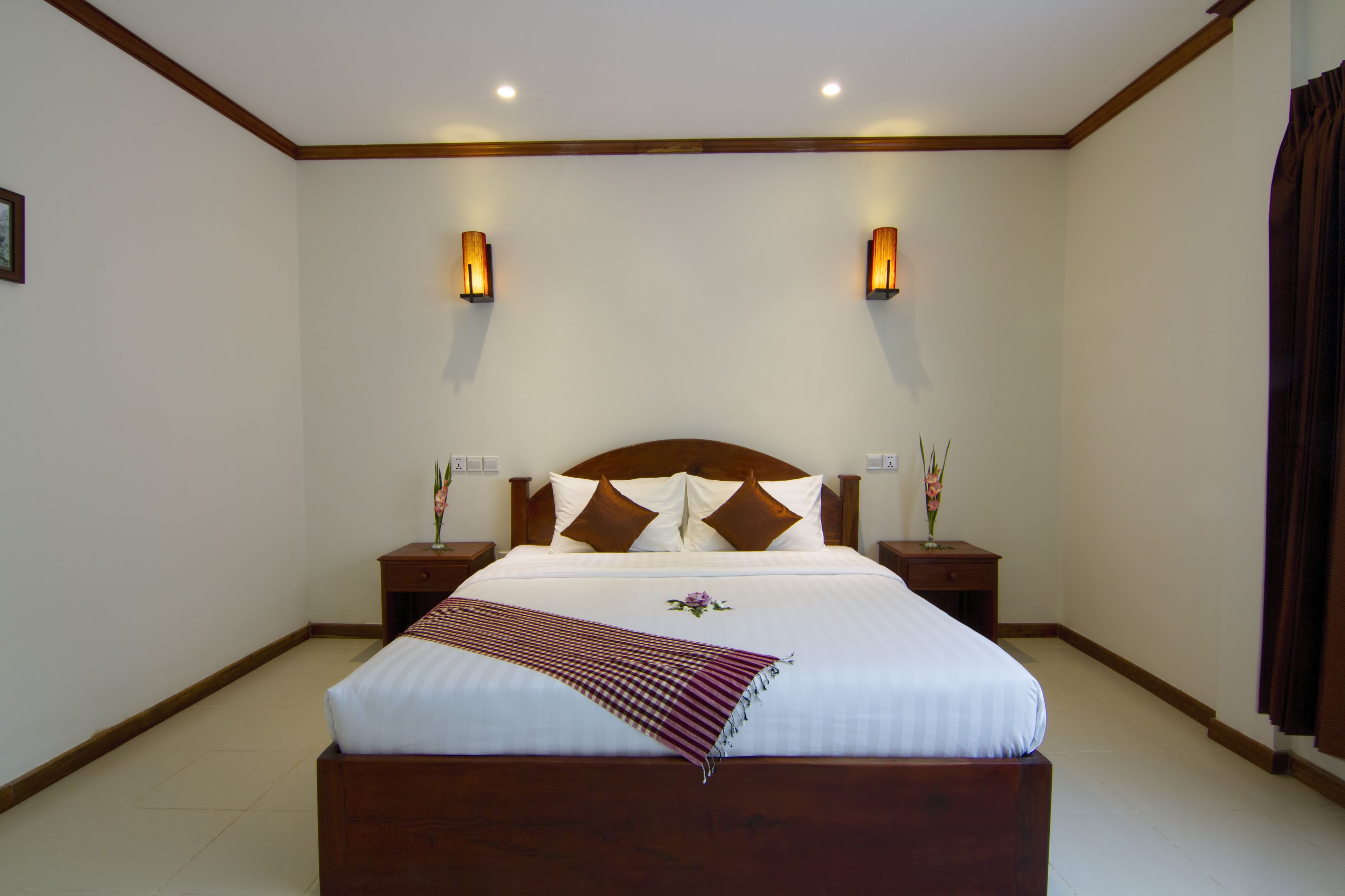 A neatly made bed with a wooden headboard, two bedside tables with lamps, and a decorative pillow arrangement.