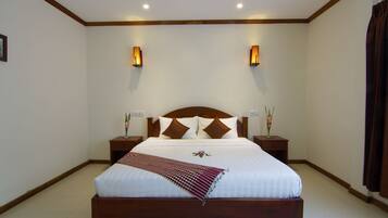Una cama bien tendida con un cabecero de madera, dos mesitas de noche con lámparas, y un arreglo decorativo de almohadas.