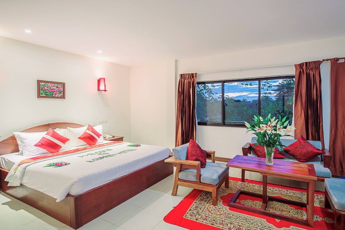 A hotel room with a bed, bedside table, chair, and a small table with a vase of flowers.