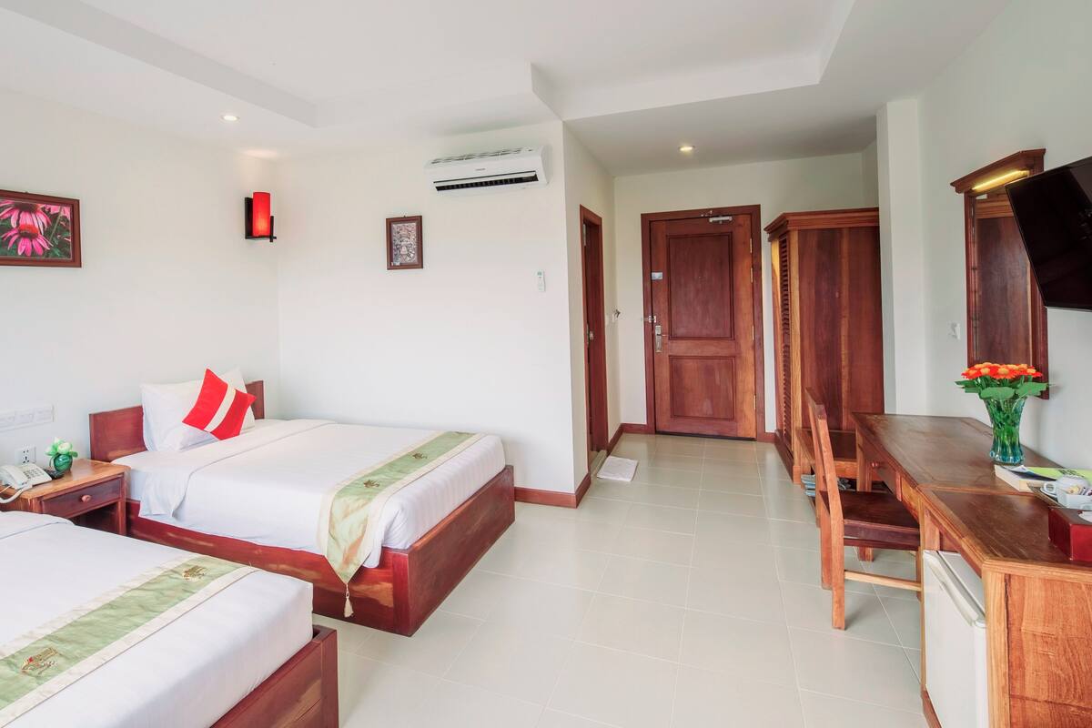 A hotel room with two beds, a desk, a chair, a TV, and an air conditioning unit.