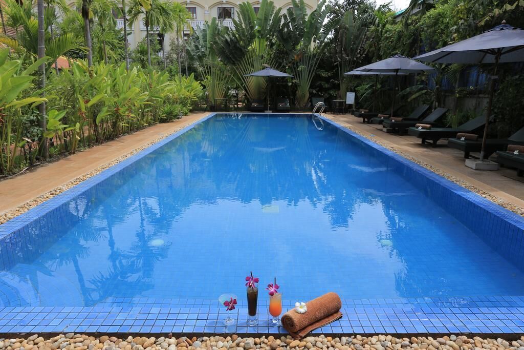 A pool with lounge chairs and umbrellas, surrounded by tropical plants.