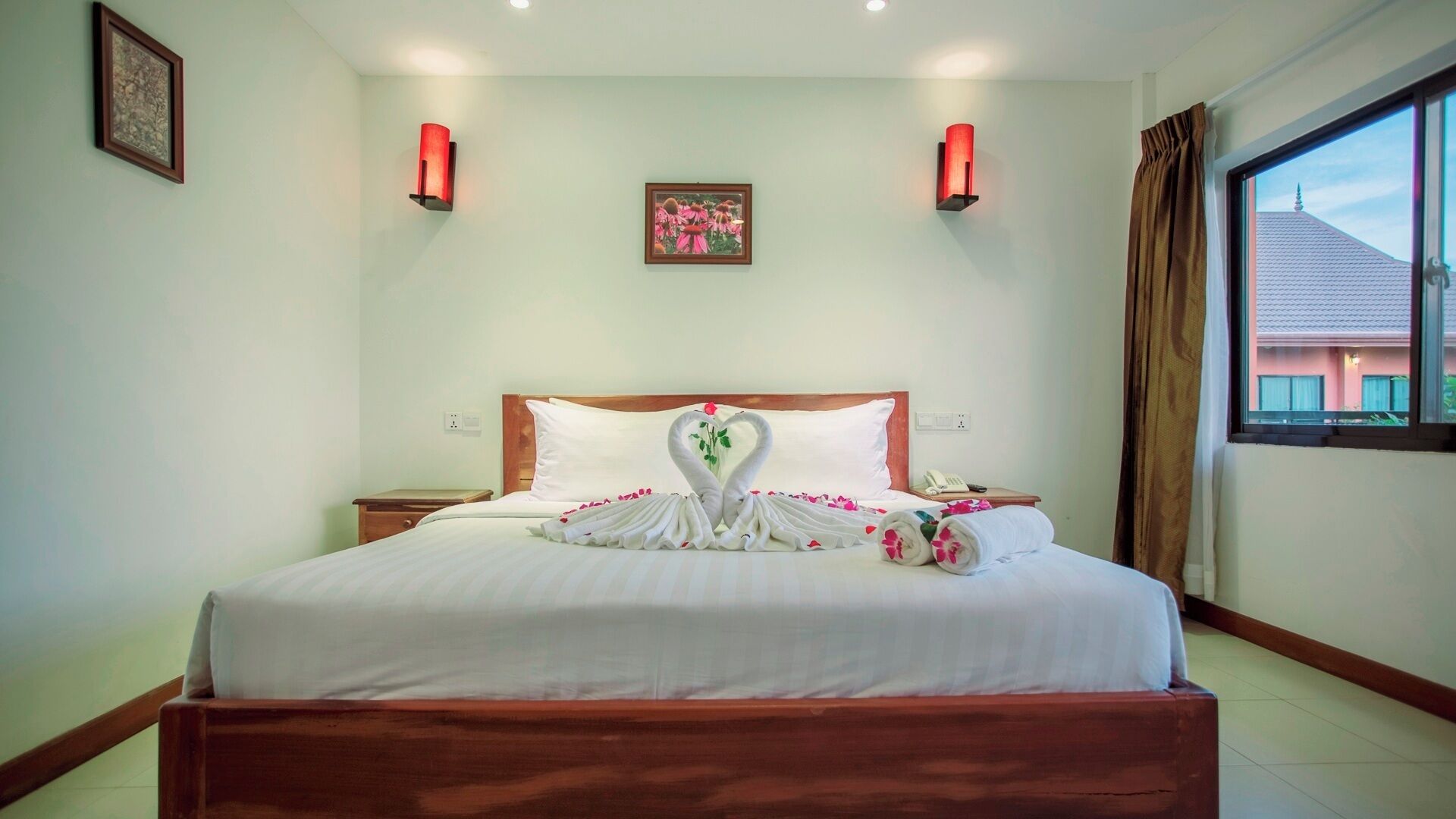 Habitación de hotel con una cama bien hecha, cabecera de madera, un cuadro enmarcado en la pared y una ventana con cortinas.