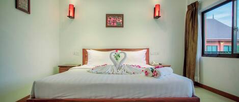 Habitación de hotel con una cama bien hecha, cabecera de madera, un cuadro enmarcado en la pared y una ventana con cortinas.