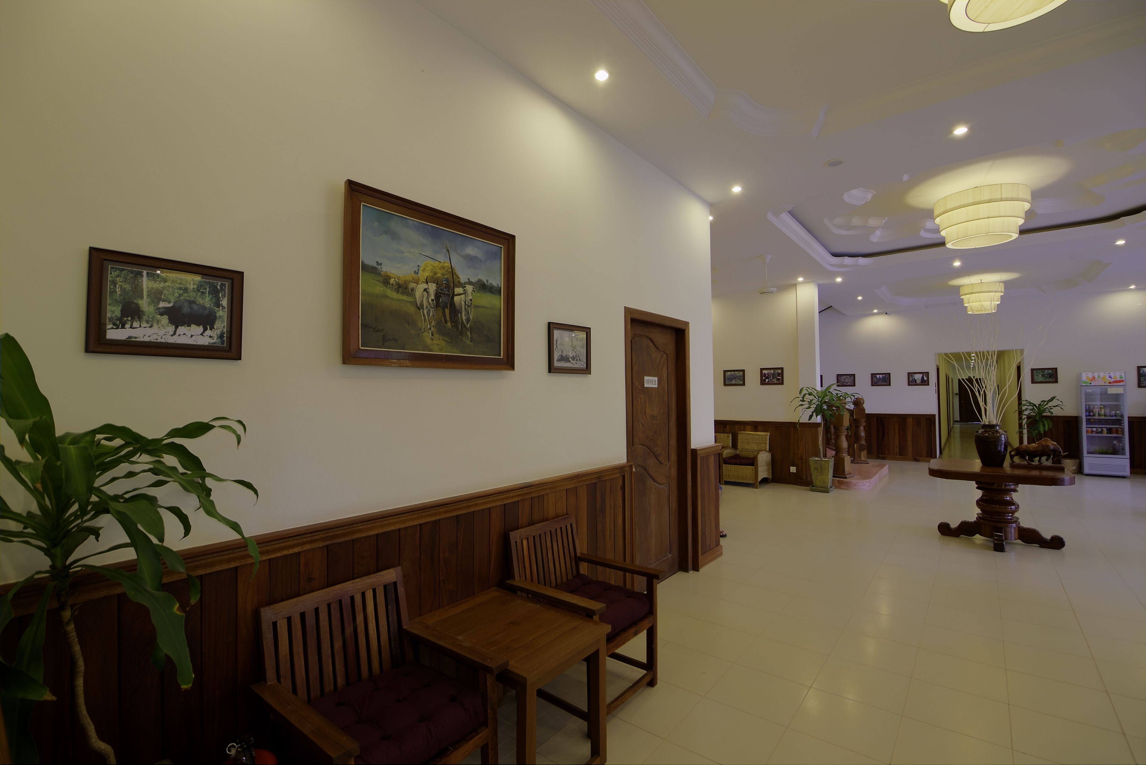 A lobby with wooden benches, framed artwork on the walls, and a potted plant.