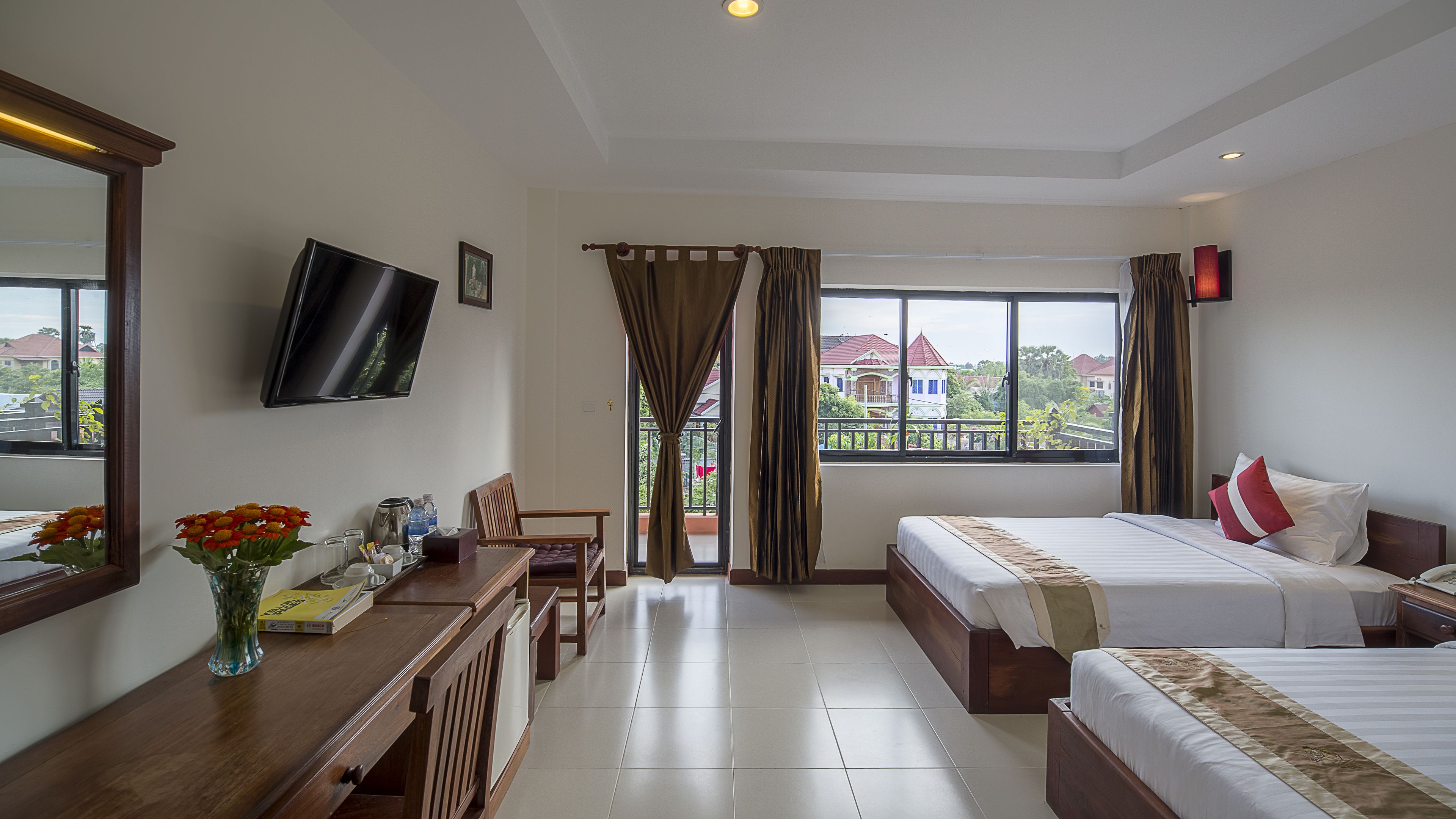 A hotel room with a bed, a desk with a computer, a TV, and a window with curtains.