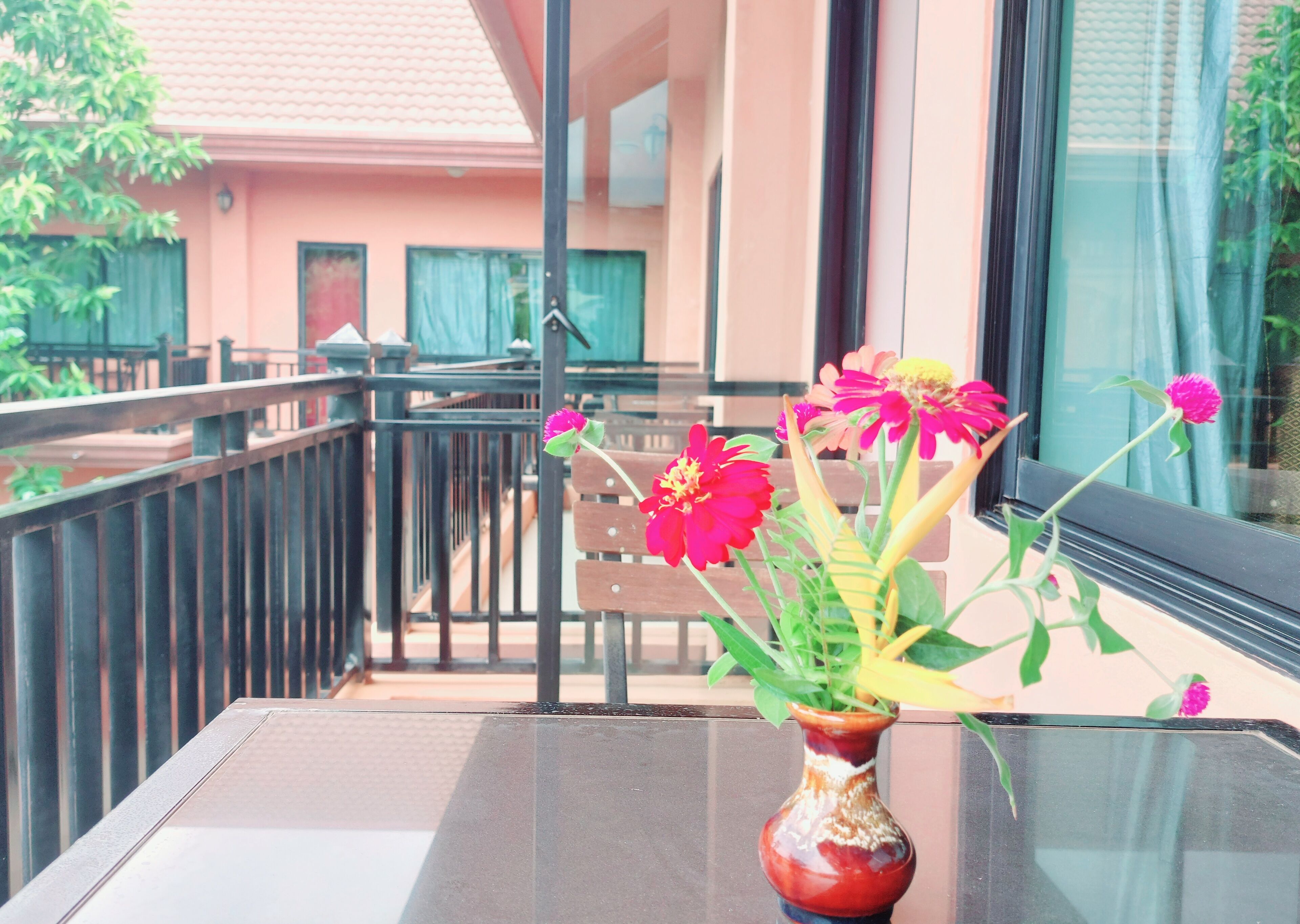 A balcony with a table, a vase with flowers, and a building in the background.