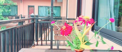 A balcony with a table, a vase with flowers, and a building in the background.