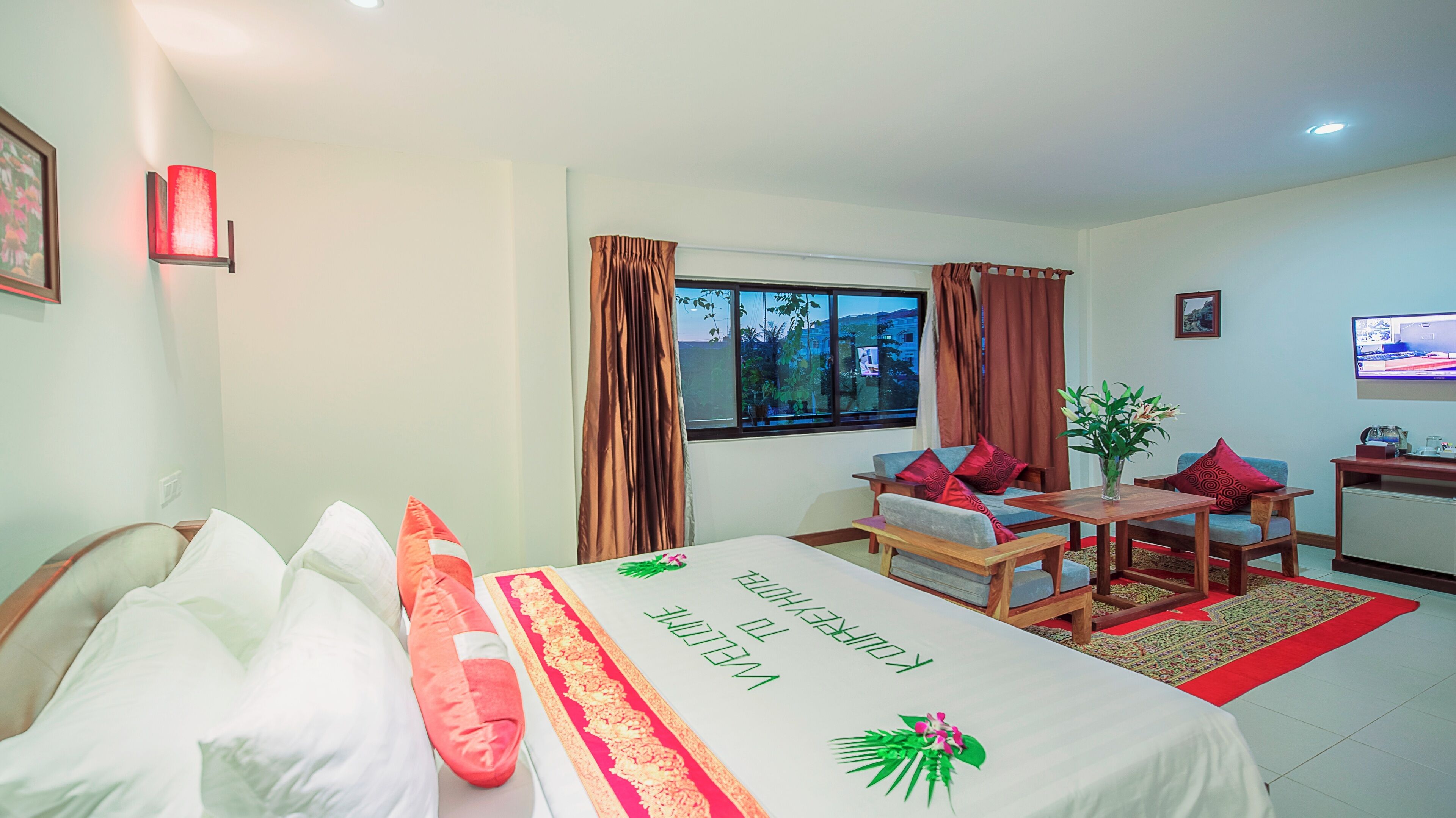 A hotel room with a bed, a sofa, a TV, and a window with curtains.