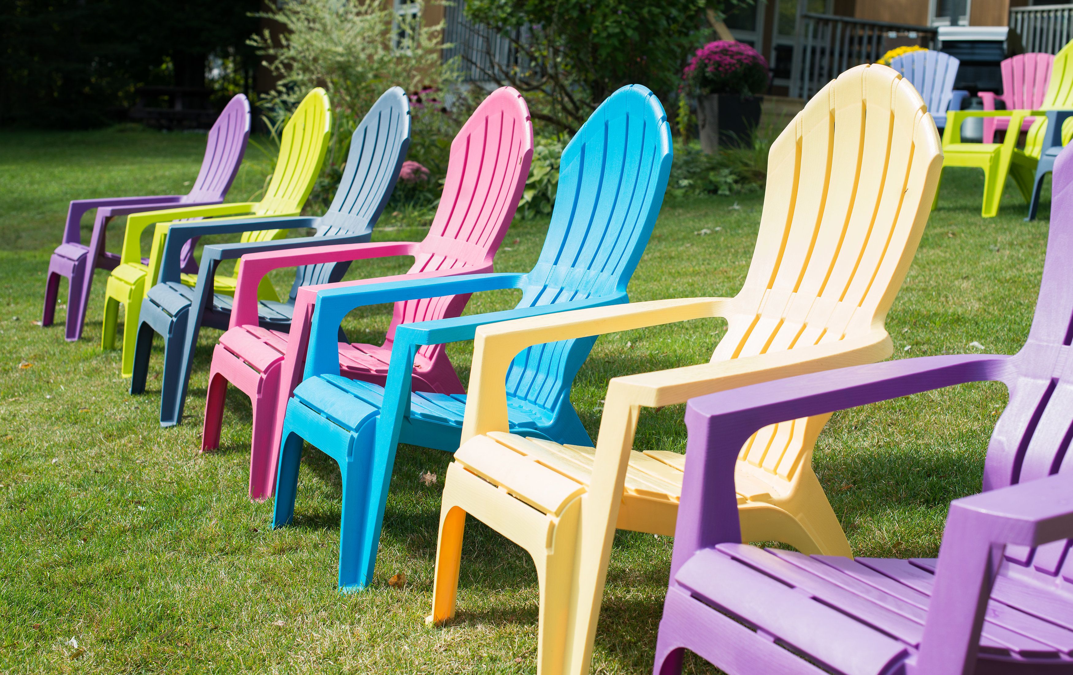 A row of colorful Adirondack chairs arranged on a grassy lawn.