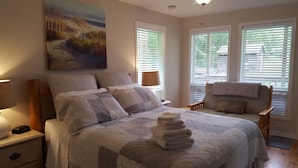 A bedroom with a large bed, a nightstand, a lamp, a chair, and a painting on the wall. - Ogopogo Resort (Minden Hills)