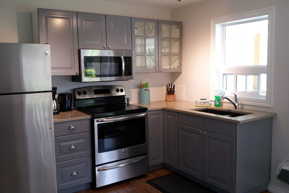 A modern kitchen with stainless steel appliances, grey cabinets, and a window providing natural light.