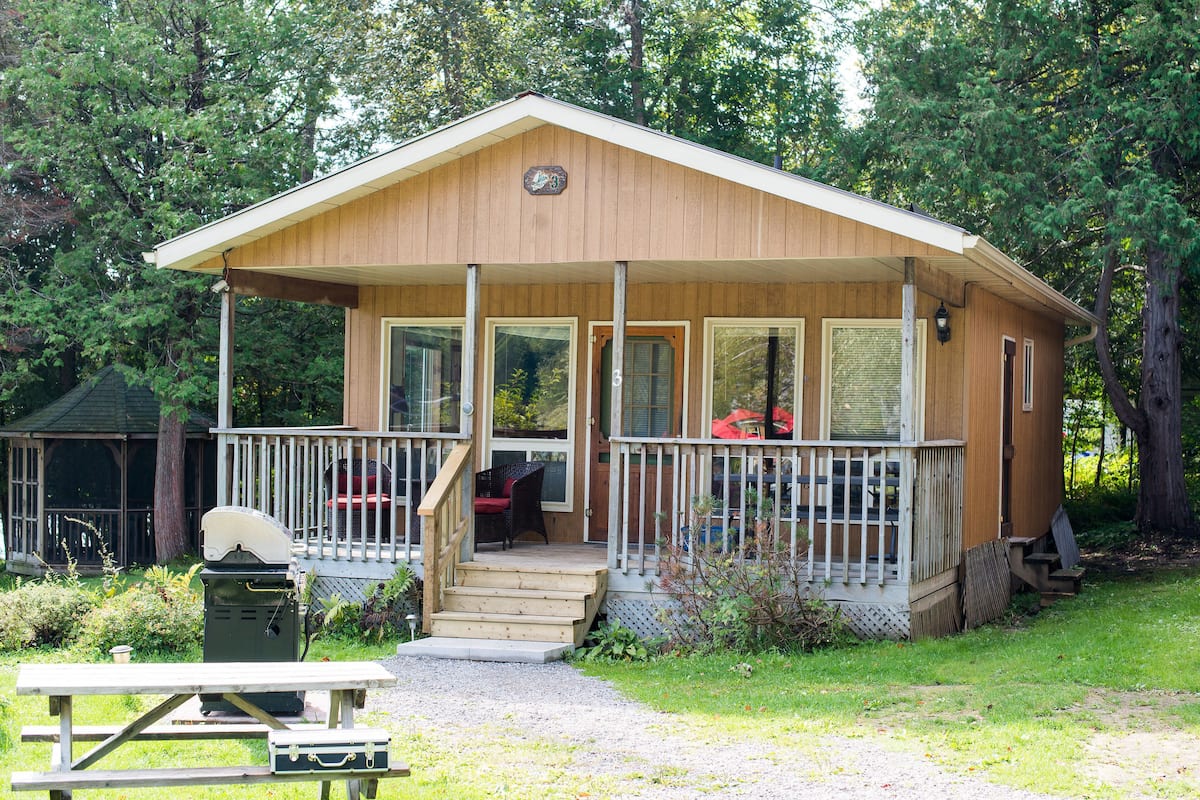 A wooden cabin with a porch, a picnic table, and a grill.
