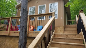 A wooden staircase leading to a deck with a railing, surrounded by trees and a building with windows. - Ogopogo Resort (Minden Hills)
