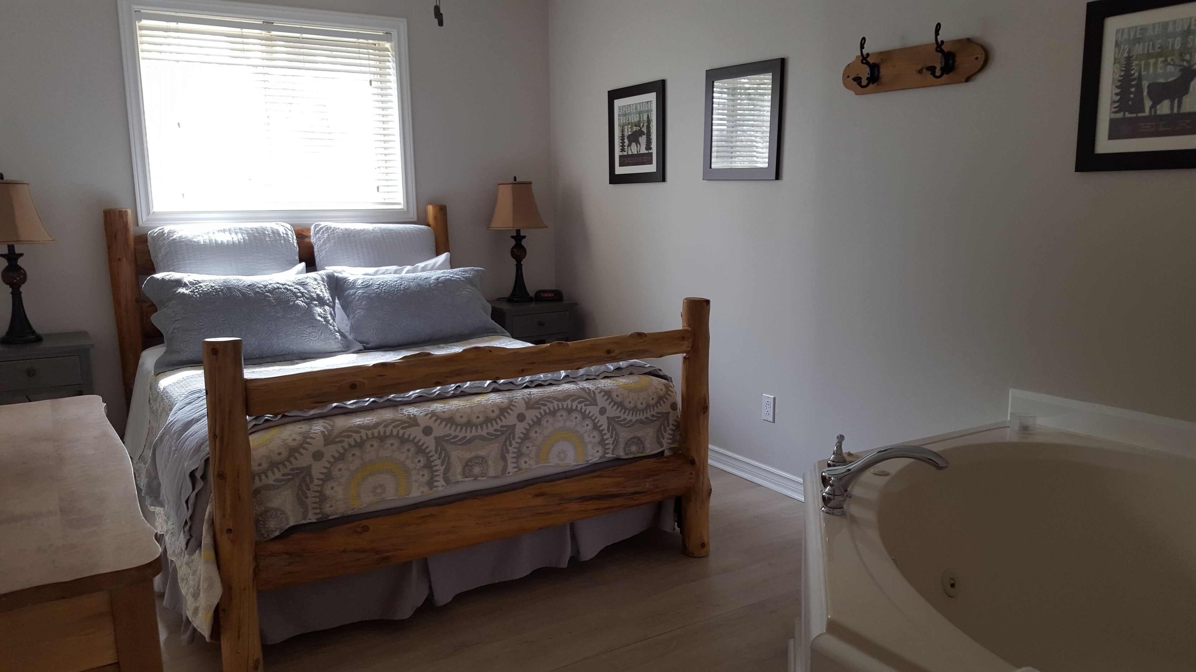 Ein Schlafzimmer mit einem hölzernen Bett, einem Nachttisch, einer Lampe, einem gerahmten Bild und einer Badewanne.