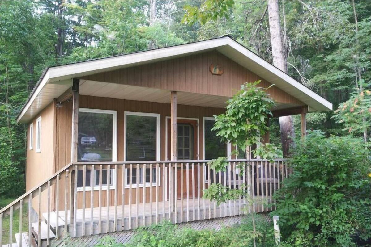 A wooden cabin with a porch, large windows, and a staircase leading to the entrance.