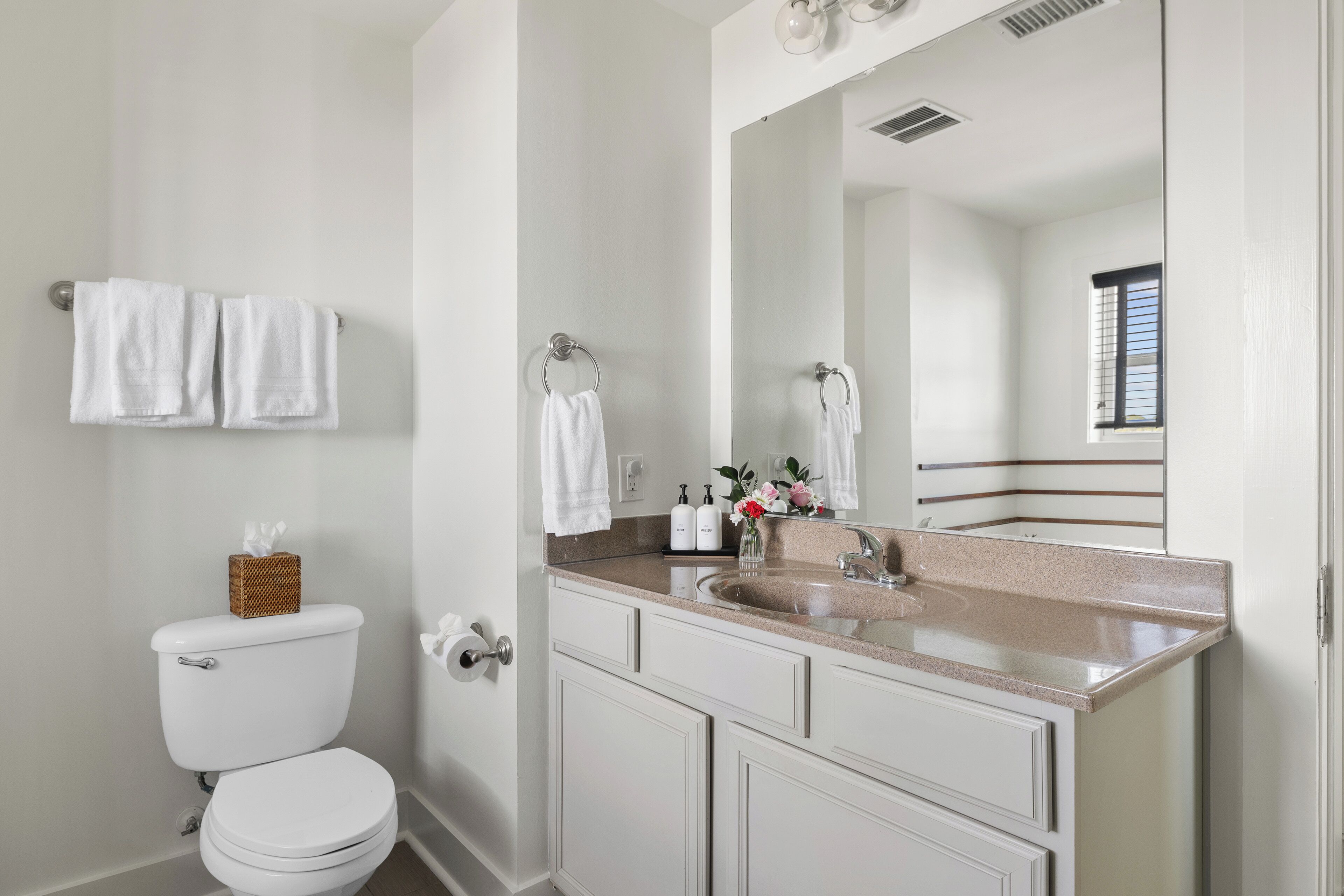 Une salle de bain avec des toilettes, un lavabo et un miroir. Des serviettes sont accrochées au mur et un panier est posé sur les toilettes.