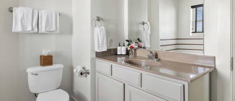 Une salle de bain avec des toilettes, un lavabo et un miroir. Des serviettes sont accrochées au mur et un panier est posé sur les toilettes.
