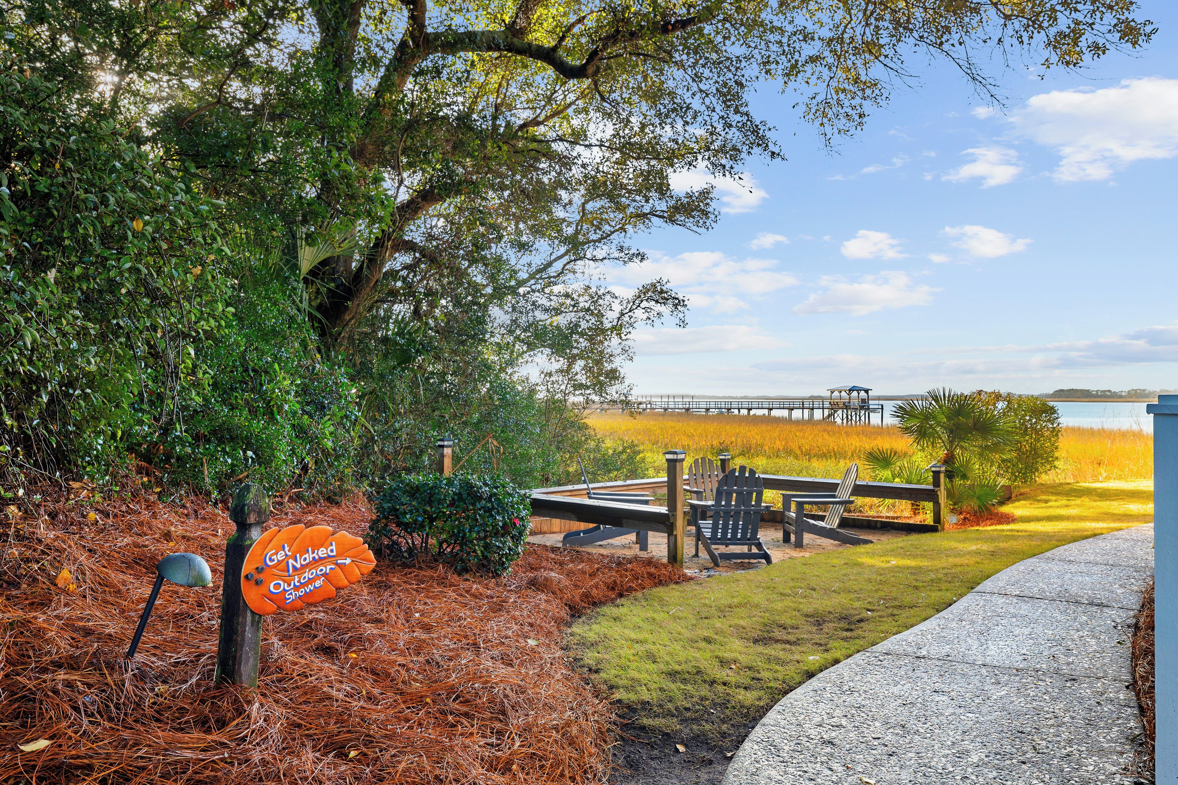 A wooden deck with outdoor seating, a sign for a 'Naked Outdoor Shower', and a view of a lake.