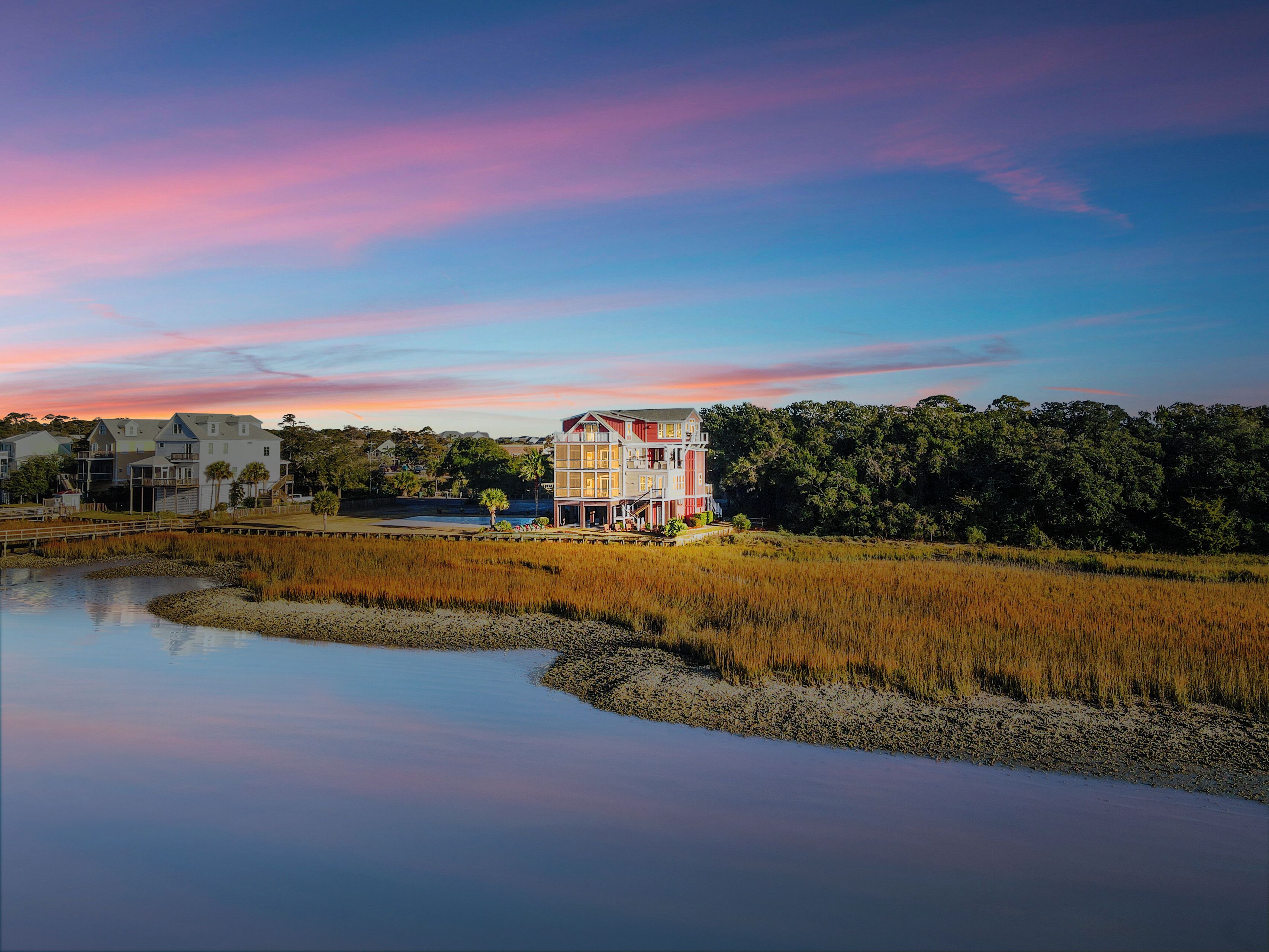 Une propriété située au bord de l’eau, avec une grande maison à plusieurs niveaux et un balcon imposant, entourée d’un paysage naturel et bordée d’une étendue d’eau calme.