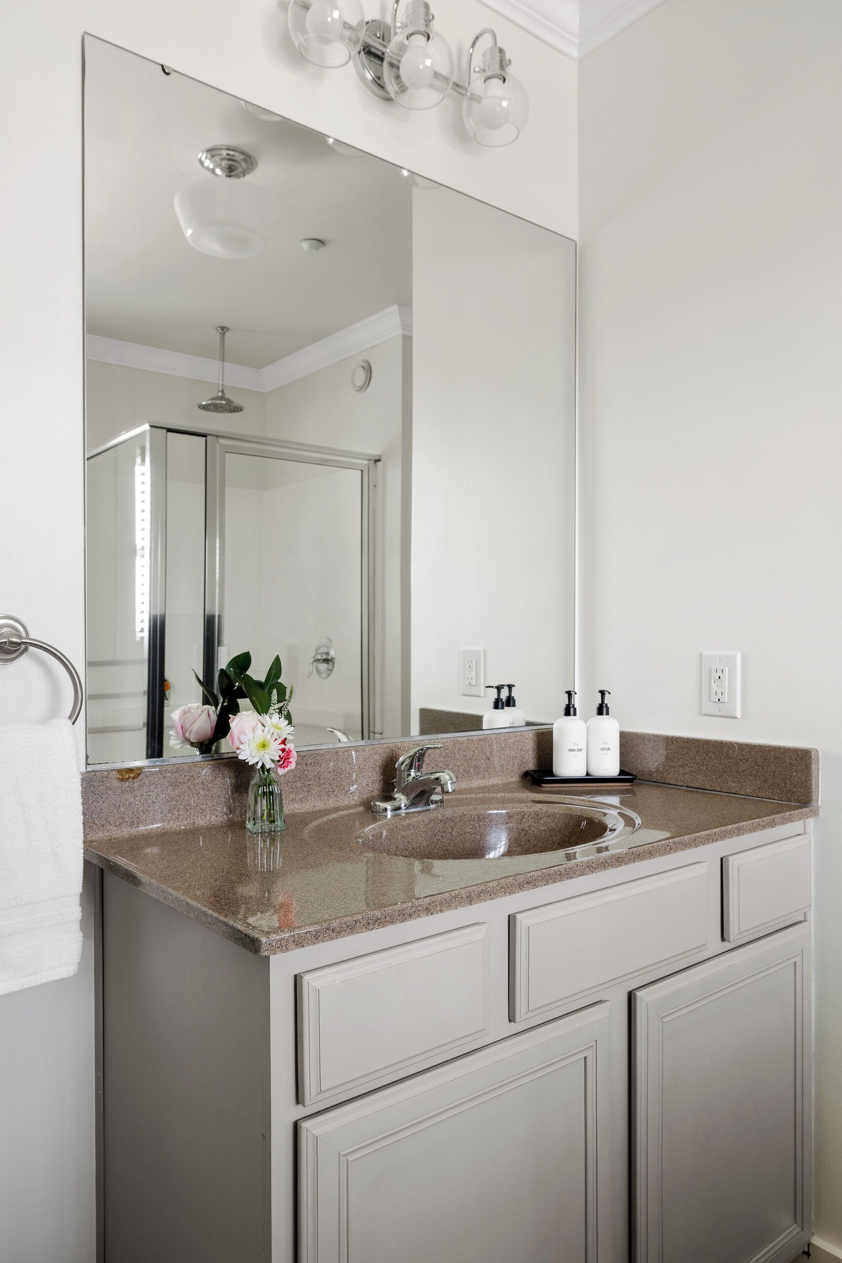 Une salle de bain avec un comptoir en granit, un grand miroir, un lavabo et deux armoires.