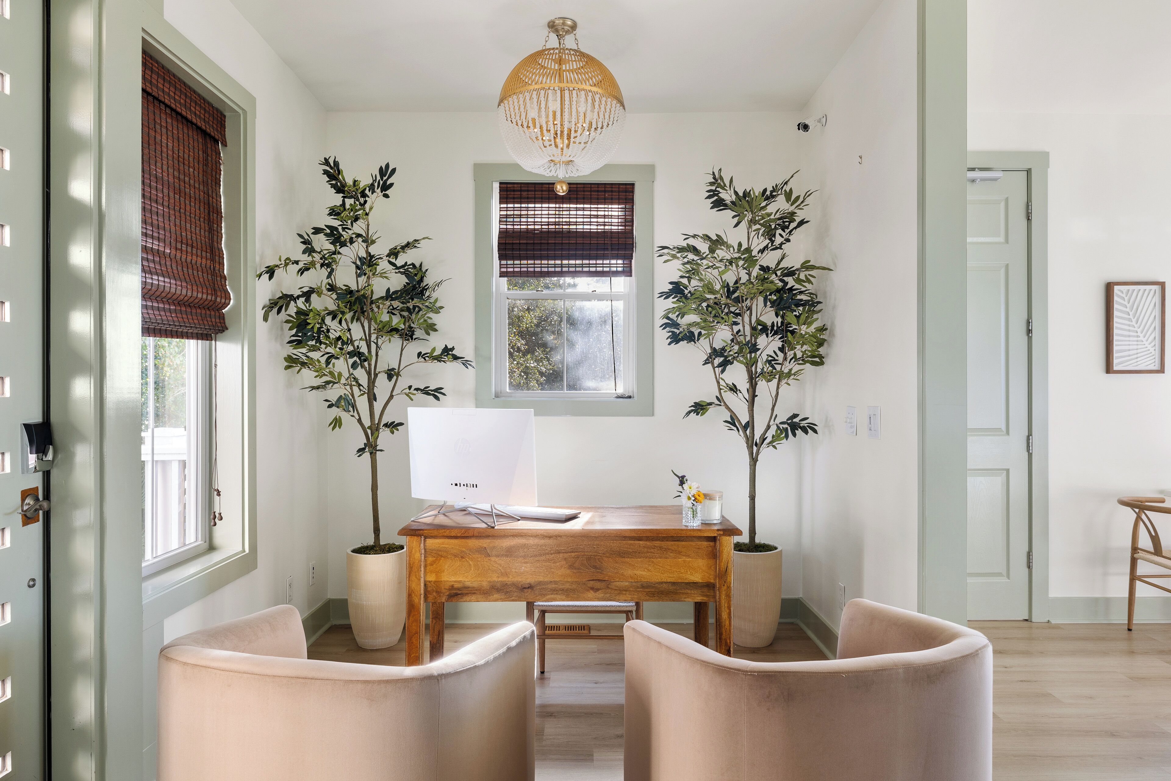 Une pièce avec un bureau en bois, deux plantes en pot, un tableau blanc et un lustre suspendu.