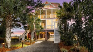 A multi-story building with a balcony, surrounded by palm trees and a gravel pathway.