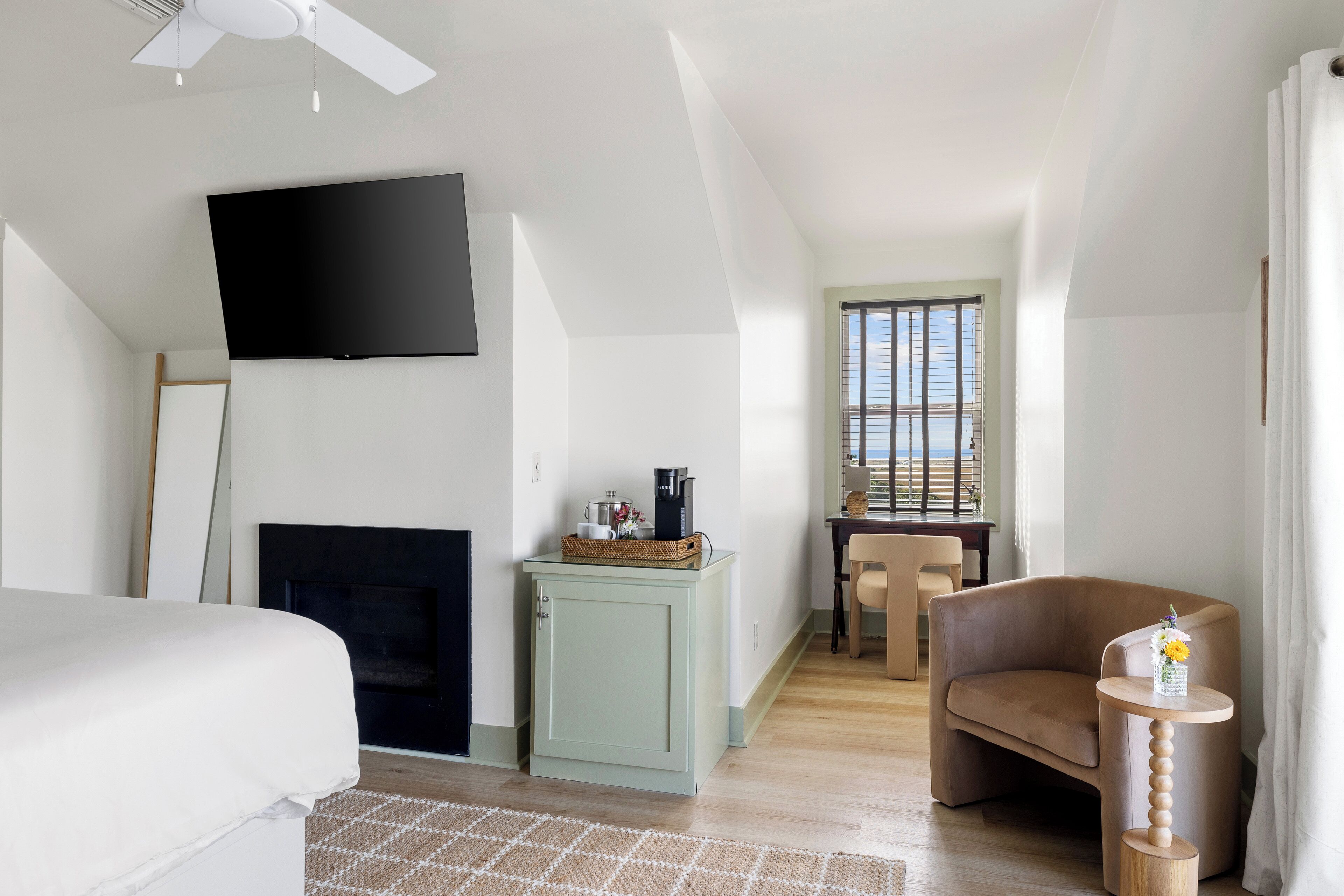 Een hotelkamer met een bed, een flatscreen televisie aan de muur, een klein kastje met een mand, een stoel en een tafel met een bloevas.