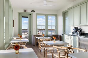 A dining area with tables and chairs, a kitchen area, and a view of the water. - Regatta Inn Folly Beach (Folly Beach)