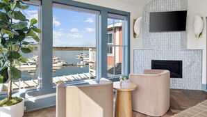 A modern living room with large windows overlooking a marina, a flat-screen TV mounted on the wall, and a fireplace.