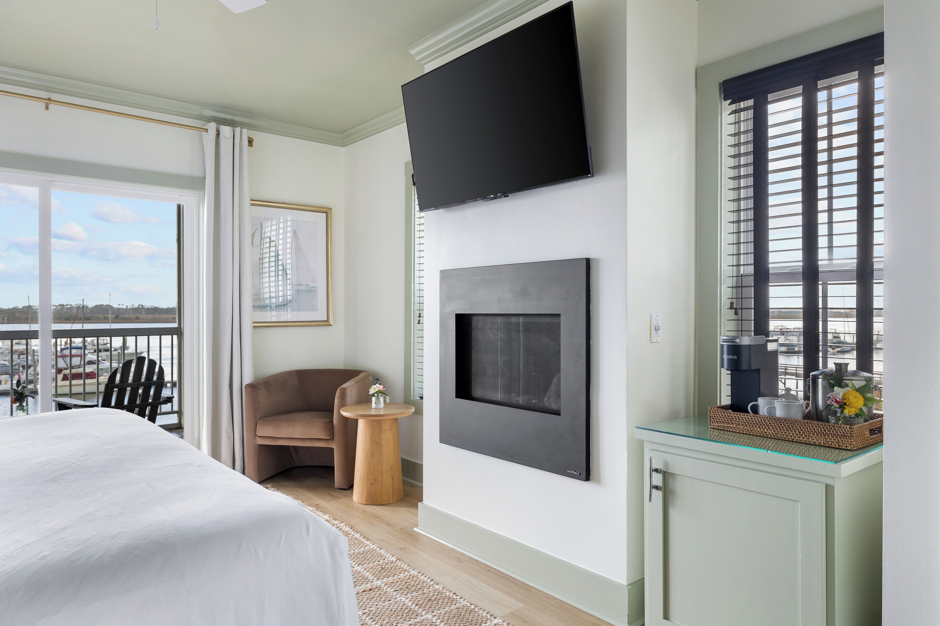 Ein Hotelzimmer mit einem großen Bett, einem an der Wand befestigten Flachbildfernseher, einem kleinen runden Tisch mit einer Vase und Blick auf die Stadt durch das Fenster.