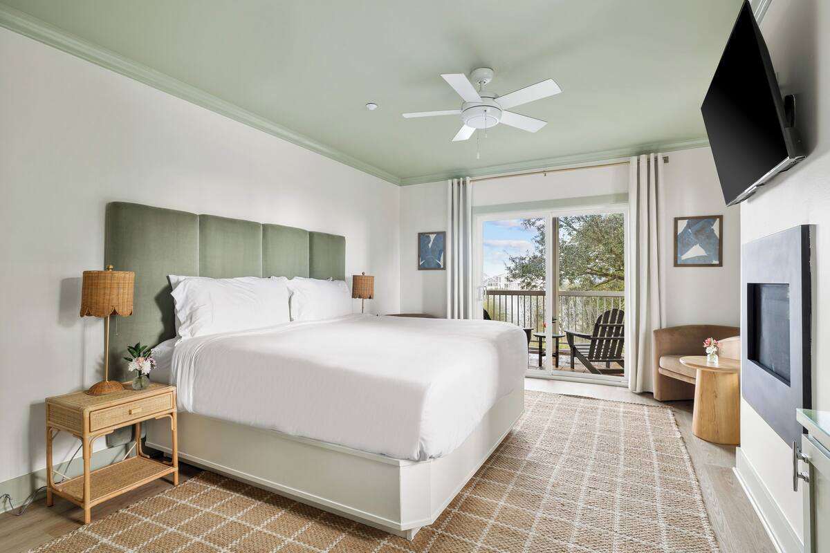 A bedroom with a bed, a ceiling fan, a TV, and a balcony with outdoor seating.