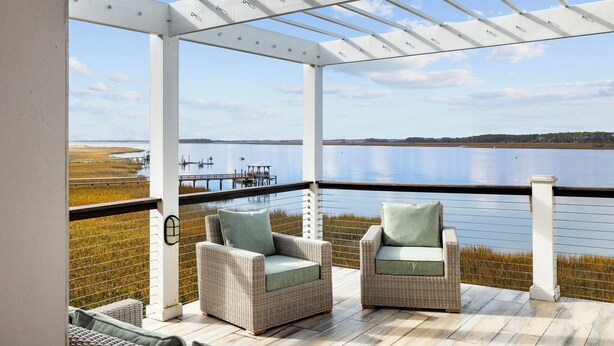 A covered outdoor seating area with wicker chairs and a view of a lake.