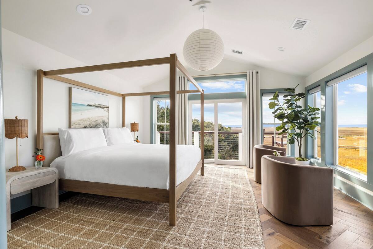 A bedroom with a four-poster bed, a large window with a view, and a potted plant.