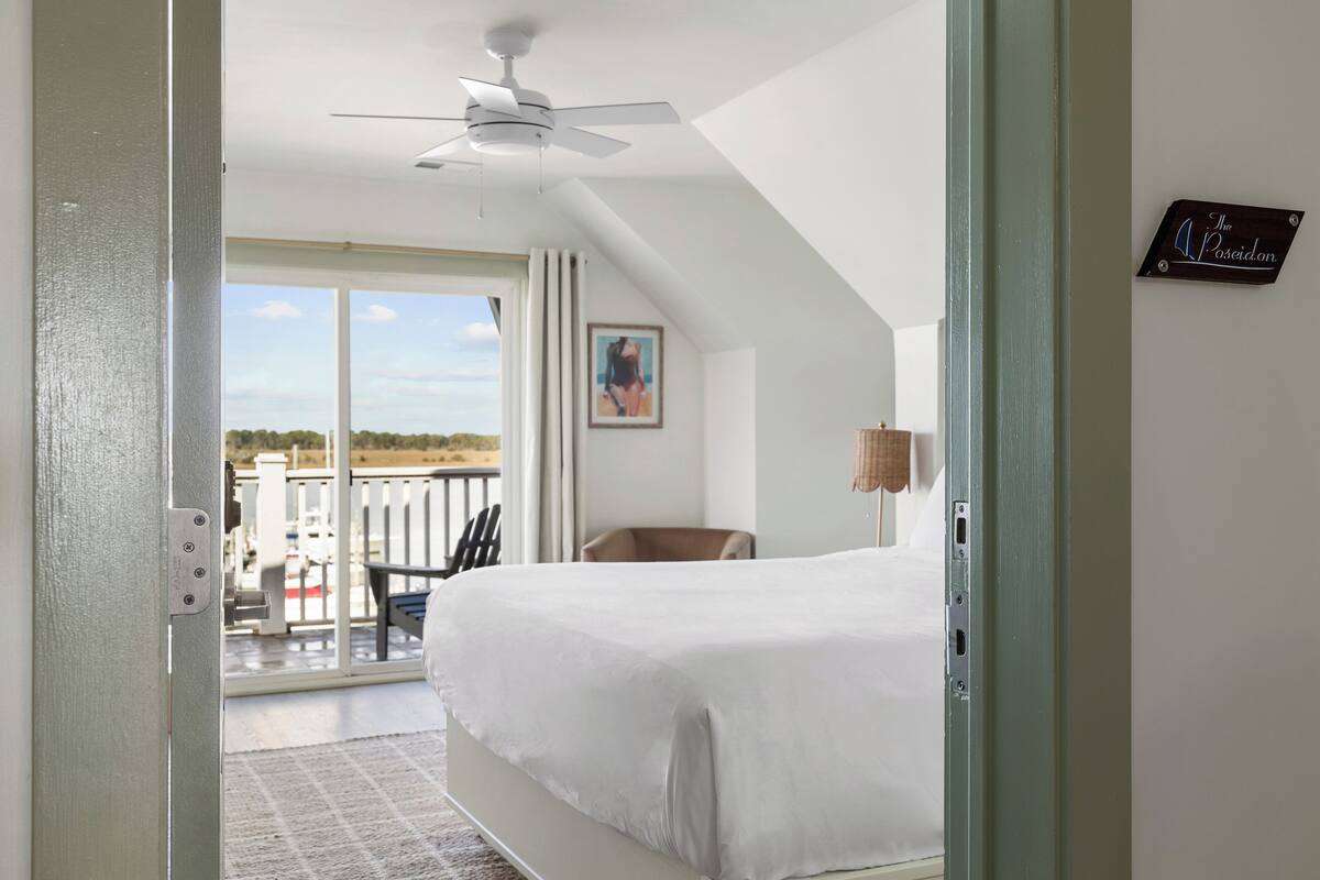 A bedroom with a bed, a ceiling fan, a balcony with a chair, and a sign on the wall.