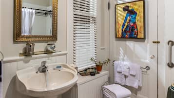 A bathroom with a white sink, a gold-framed mirror, white towels, and a painting on the wall.