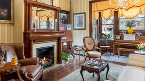 Ein gemütliches Wohnzimmer mit Kamin, Ledersesseln, einem Klavier und einem großen Fenster mit Vorhängen.