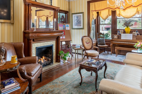 Una sala de estar acogedora con chimenea, sillones de cuero, un piano y un amplio ventanal con cortinas.