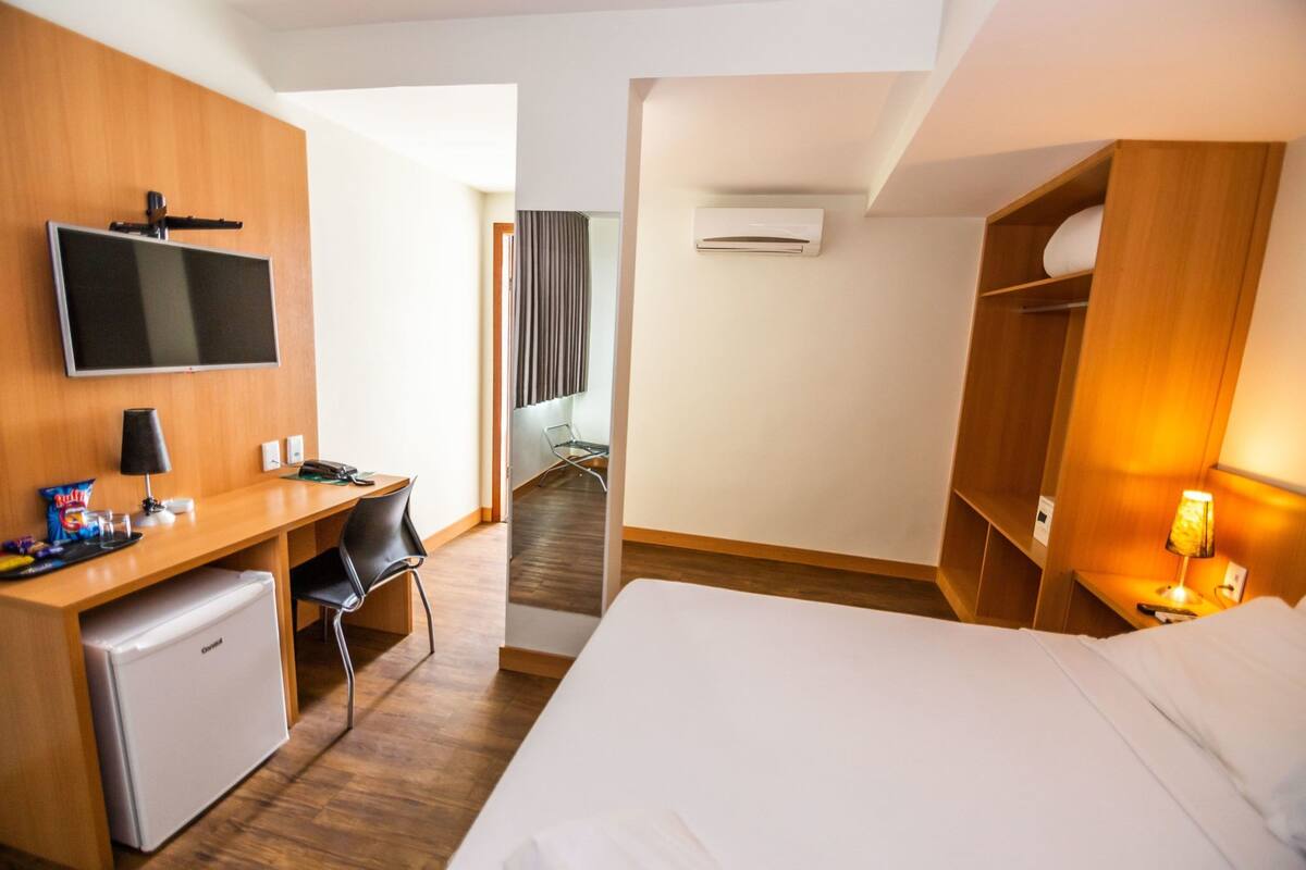 Habitación de hotel con cama, escritorio, silla y televisión montada en la pared.