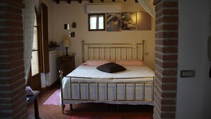 Un dormitorio con una cama de estructura metálica, pared de ladrillo, ventana y aire acondicionado de pared.