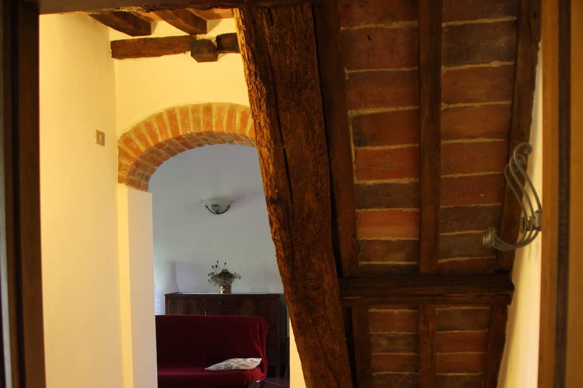 A hallway with a tiled floor, a red sofa, a wooden ceiling, and a brick archway.