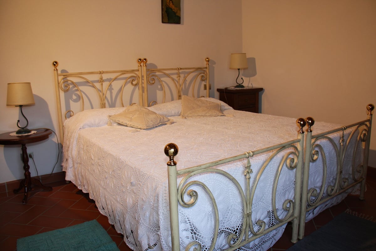 A neatly made bed with a metal frame and white bedding, two bedside tables with lamps, and a green rug on the floor.