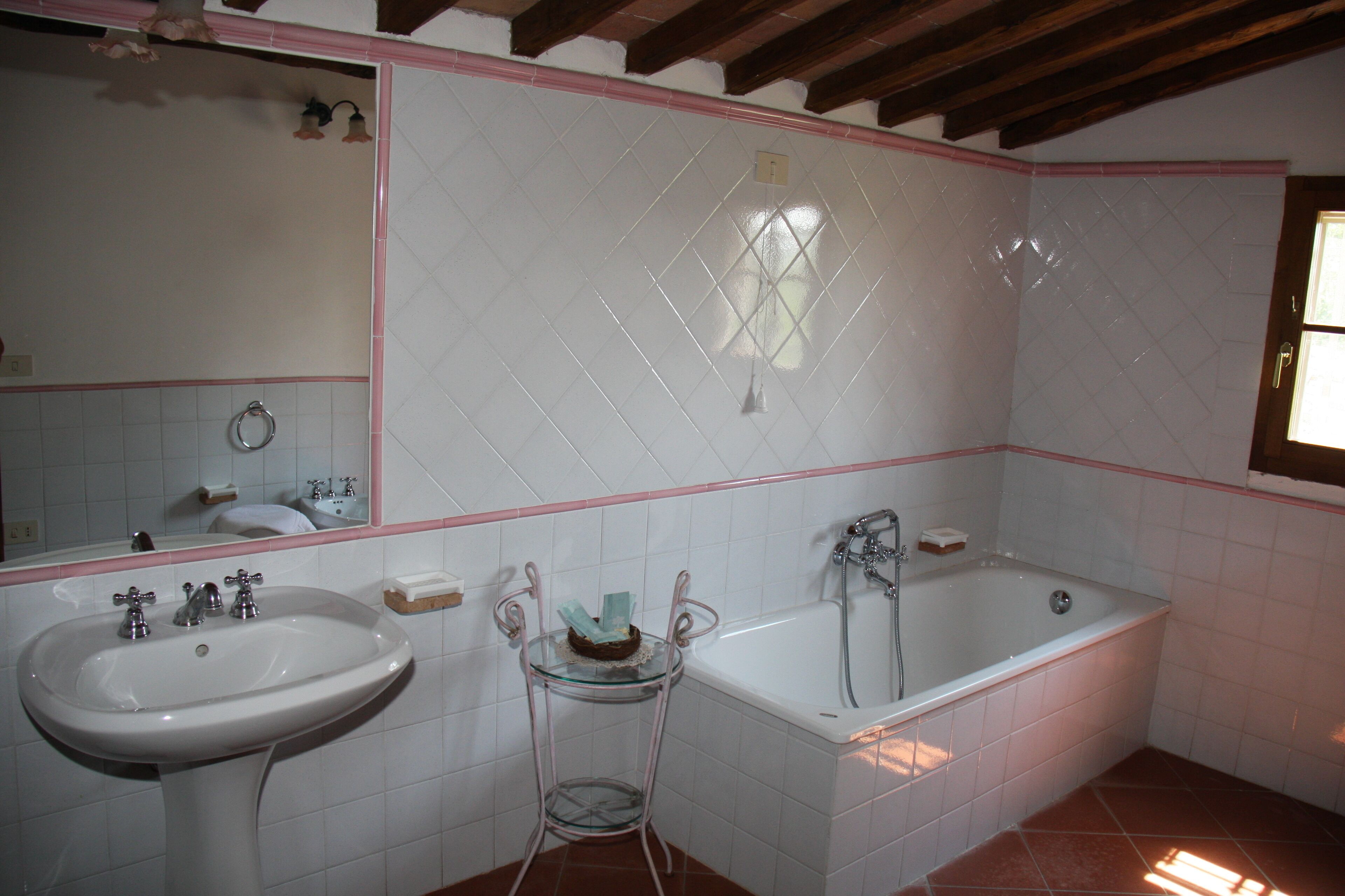 A bathroom with a white sink, a glass shelf, a bathtub, and a mirror.