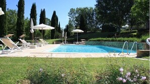 Piscina con sillas de descanso y sombrillas, rodeada de vegetación y árboles.